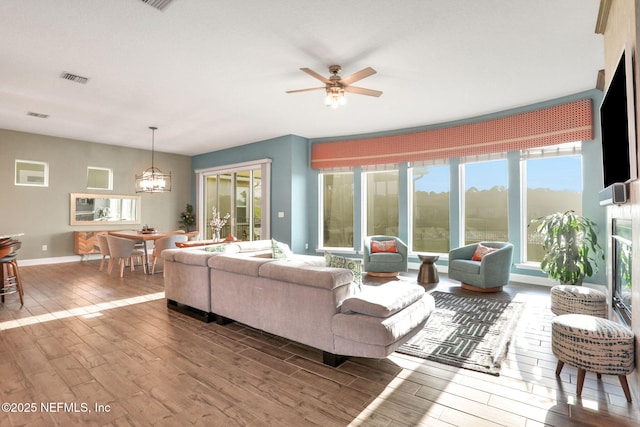 living area featuring visible vents, baseboards, wood finished floors, and ceiling fan with notable chandelier