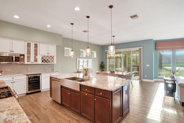 kitchen with a sink, visible vents, light wood-type flooring, wine cooler, and backsplash
