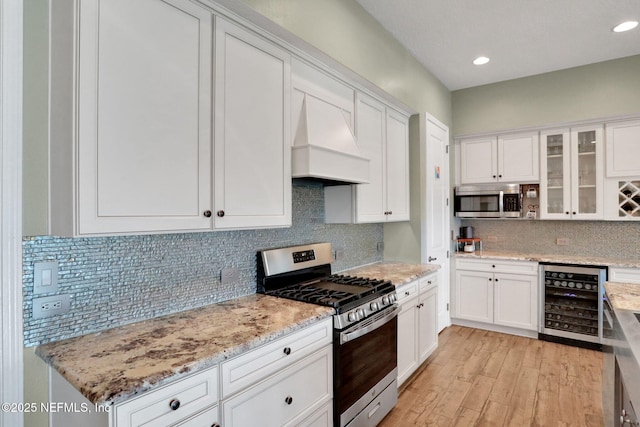 kitchen featuring tasteful backsplash, stainless steel appliances, custom range hood, white cabinetry, and wine cooler