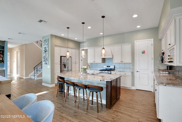 kitchen with a kitchen island with sink, appliances with stainless steel finishes, backsplash, light wood finished floors, and visible vents