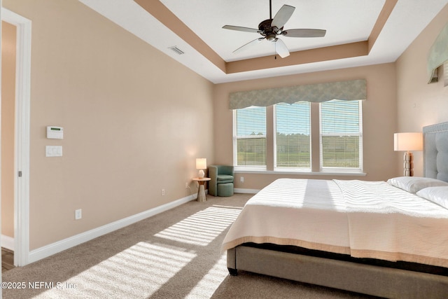 bedroom featuring visible vents, a tray ceiling, baseboards, carpet, and a ceiling fan