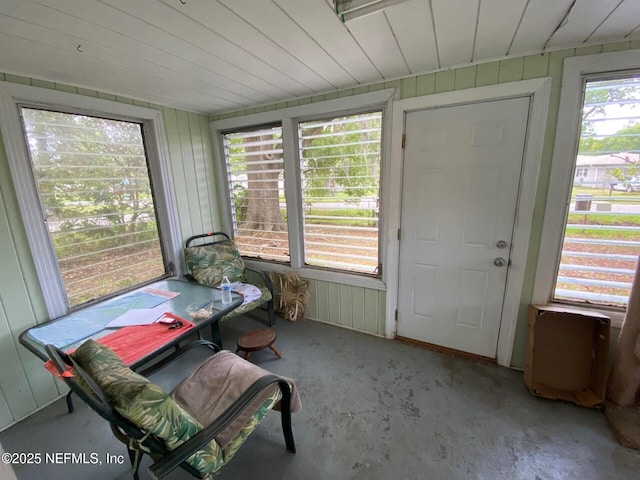 sunroom / solarium with wood walls and unfinished concrete floors