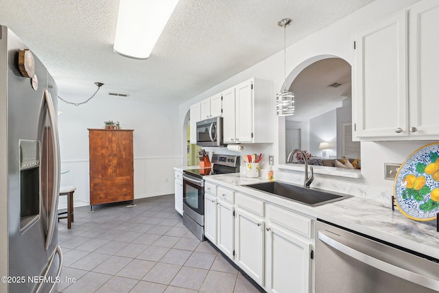 4518 Mountain Brook Ln E, Jacksonville, FL 32224 - kitchen featuring stainless steel appliances, arched walkways, a textured ceiling, white cabinetry, and light tile patterned flooring