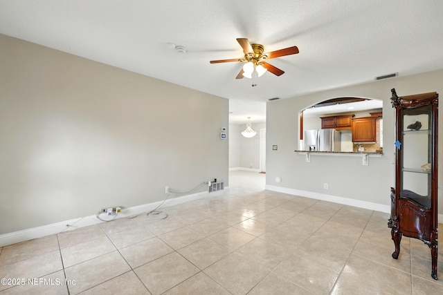 unfurnished living room with visible vents, light tile patterned flooring, baseboards, arched walkways, and a ceiling fan