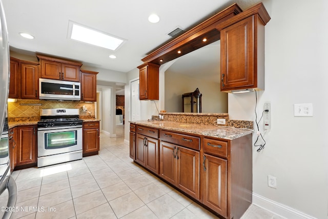 kitchen featuring decorative backsplash, visible vents, appliances with stainless steel finishes, light stone countertops, and baseboards