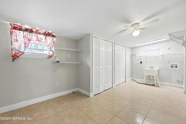 interior space featuring tile patterned flooring, baseboards, hookup for a washing machine, a textured ceiling, and a ceiling fan