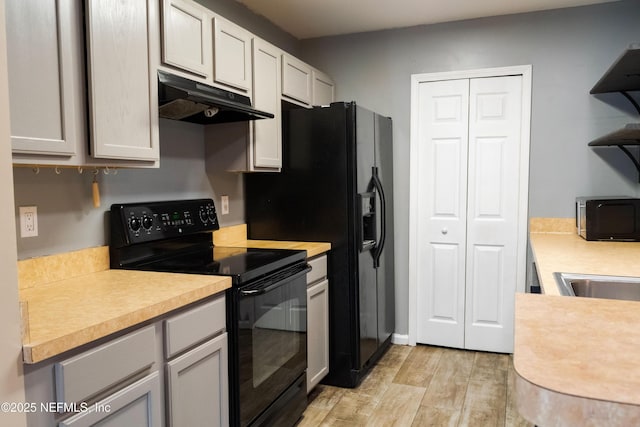 kitchen featuring black appliances, light wood finished floors, under cabinet range hood, and light countertops