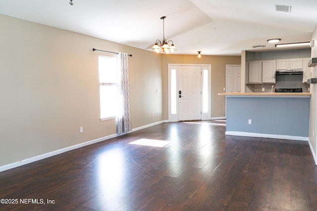 unfurnished living room with a notable chandelier, dark wood-type flooring, visible vents, baseboards, and lofted ceiling