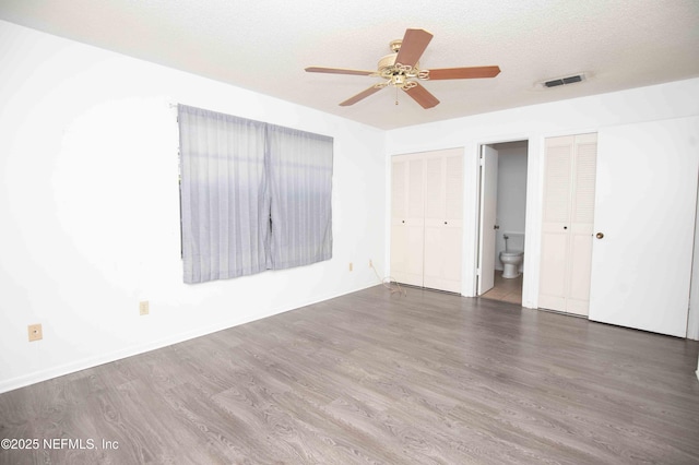 unfurnished bedroom with two closets, a ceiling fan, visible vents, wood finished floors, and ensuite bathroom