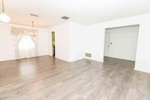 spare room featuring visible vents, wood finished floors, and a notable chandelier