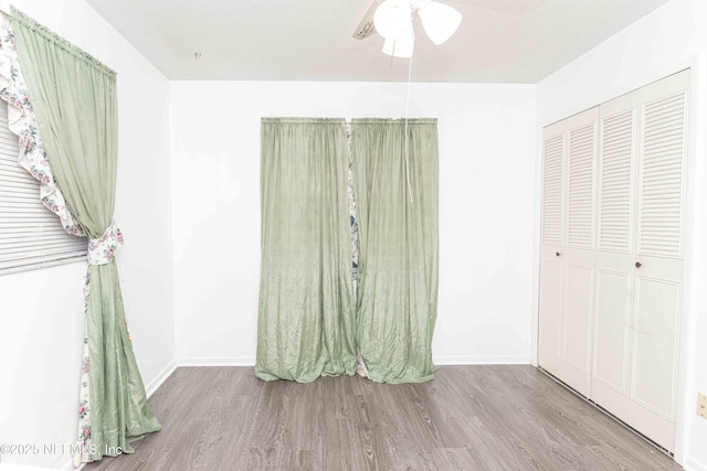 unfurnished bedroom featuring wood finished floors, a closet, a ceiling fan, and baseboards