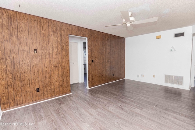 unfurnished room featuring visible vents, wood finished floors, ceiling fan, and wooden walls