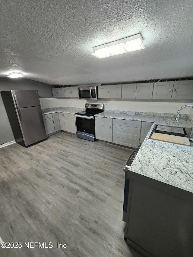 kitchen featuring a textured ceiling, appliances with stainless steel finishes, light wood-style flooring, and a sink
