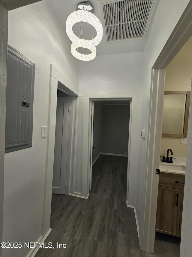 hallway featuring dark wood finished floors, a chandelier, electric panel, a sink, and visible vents