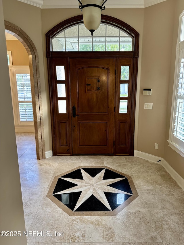 entryway with crown molding, arched walkways, and baseboards