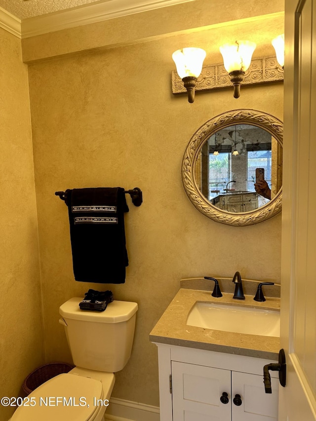 half bathroom with vanity, ornamental molding, baseboards, and toilet