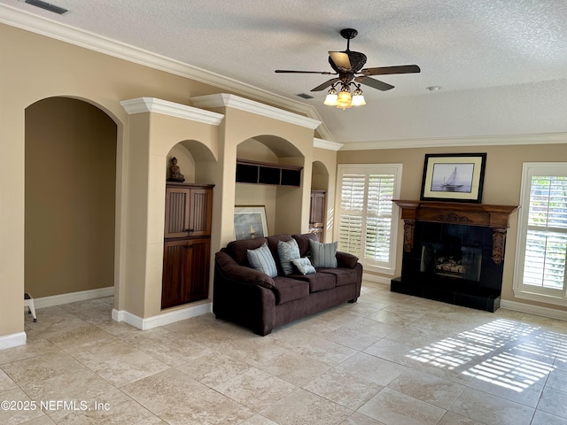 living room with ornamental molding, a glass covered fireplace, baseboards, a textured ceiling, and a ceiling fan