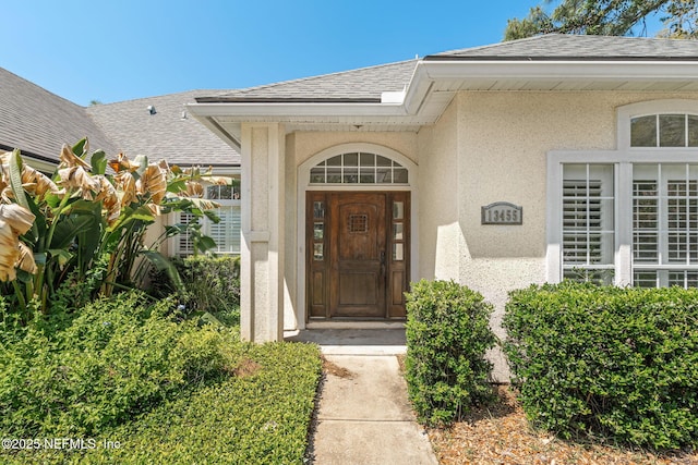 view of exterior entry featuring roof with shingles and stucco siding