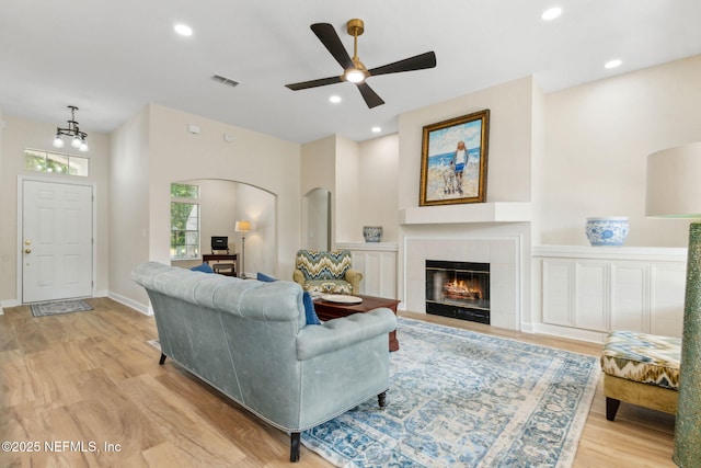 living room with ceiling fan, visible vents, arched walkways, a tile fireplace, and light wood-style flooring