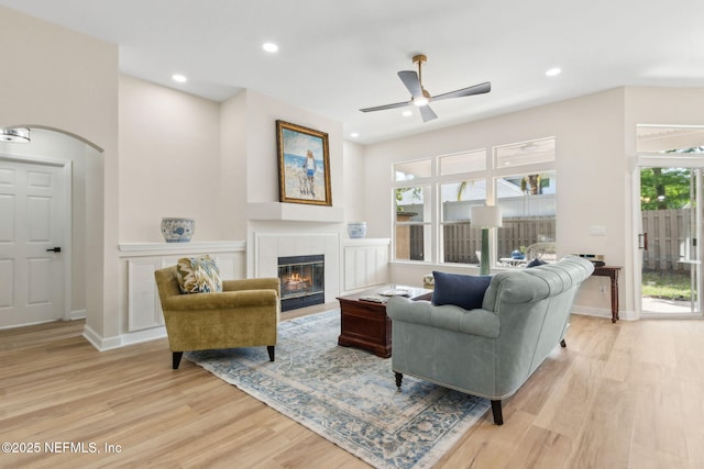 living area featuring a tiled fireplace, a ceiling fan, light wood-style flooring, and a wealth of natural light