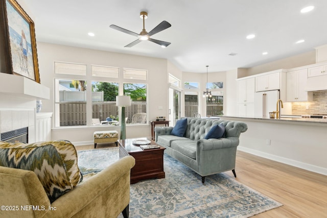 living room with a fireplace, light wood-style flooring, ceiling fan with notable chandelier, recessed lighting, and baseboards