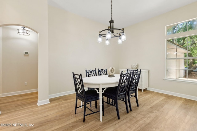 dining space featuring light wood-type flooring, arched walkways, baseboards, and a chandelier