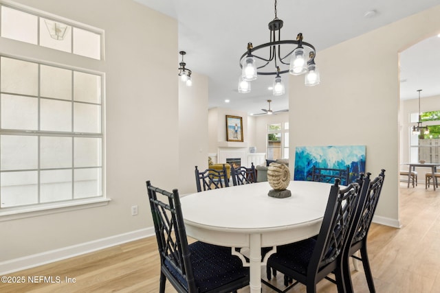 dining space featuring arched walkways, a lit fireplace, ceiling fan with notable chandelier, and light wood-style flooring