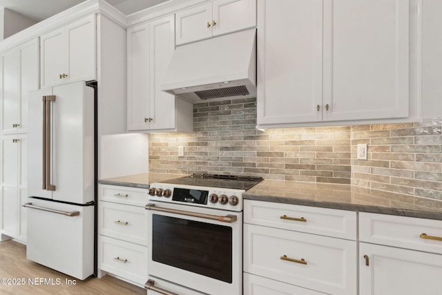 kitchen featuring white appliances, stone countertops, light wood-style floors, white cabinetry, and custom range hood