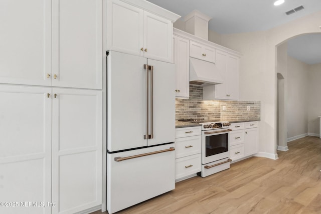 kitchen with white appliances, arched walkways, white cabinetry, backsplash, and custom exhaust hood