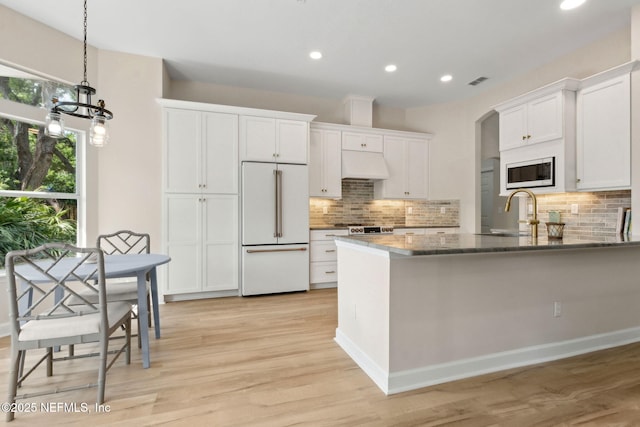 kitchen featuring decorative backsplash, high end fridge, premium range hood, built in microwave, and a sink
