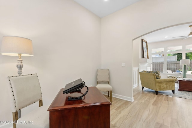 office area featuring arched walkways, baseboards, a ceiling fan, and wood finished floors