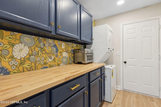 clothes washing area with cabinet space, stacked washing maching and dryer, light wood-style flooring, recessed lighting, and a toaster