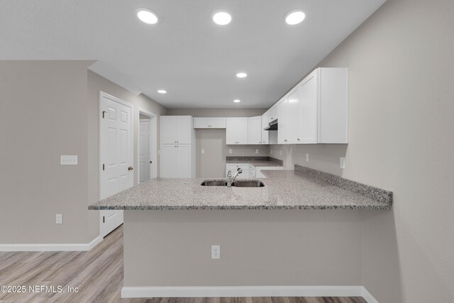kitchen featuring light stone counters, a sink, a peninsula, baseboards, and white cabinetry