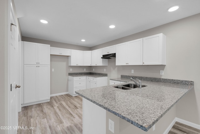 kitchen with light wood-style floors, a sink, baseboards, and a peninsula