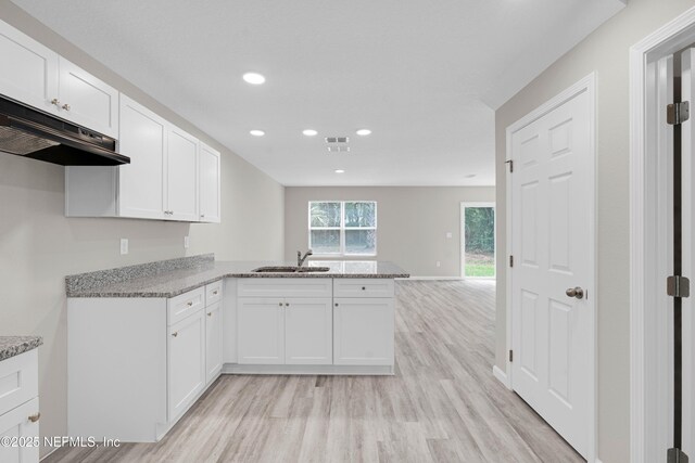 kitchen featuring a peninsula, a sink, light wood-style flooring, and visible vents