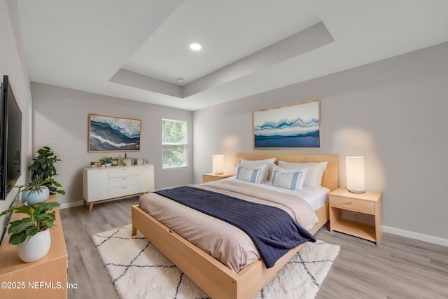 bedroom with baseboards, recessed lighting, light wood-style flooring, and a raised ceiling