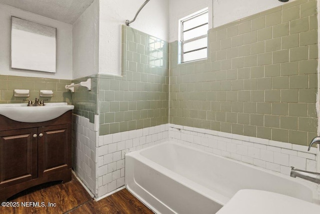 bathroom with wood finished floors, wainscoting, tile walls, shower / bathtub combination, and vanity