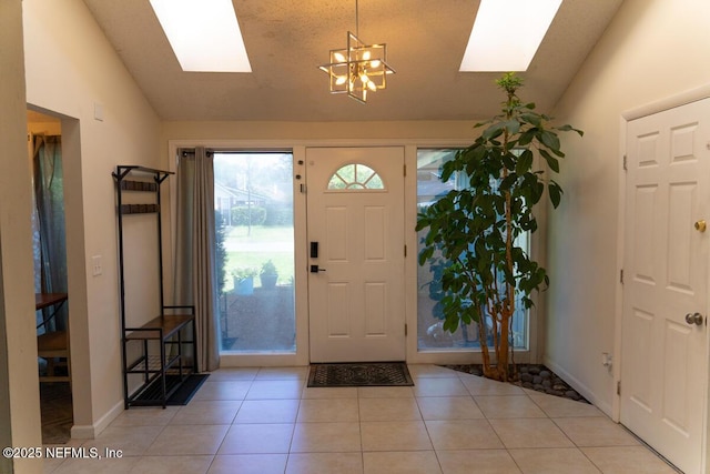 entrance foyer with baseboards, light tile patterned floors, a chandelier, and vaulted ceiling with skylight