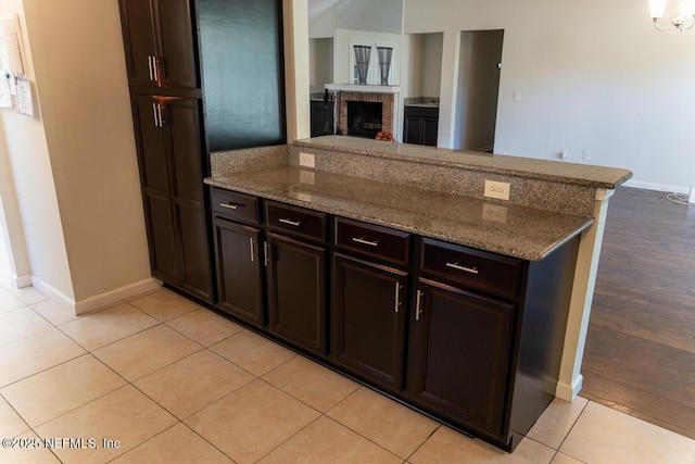 kitchen with baseboards, a brick fireplace, stone countertops, and a peninsula