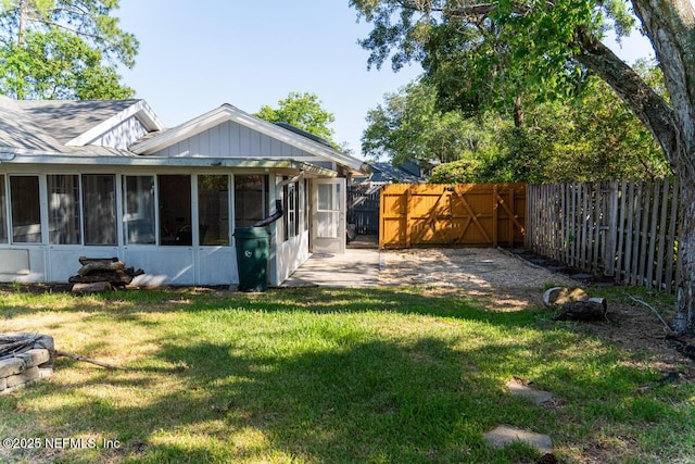back of house with a lawn, a sunroom, a fenced backyard, a patio, and a shingled roof