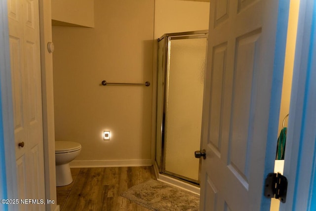 bathroom with baseboards, a stall shower, toilet, and wood finished floors