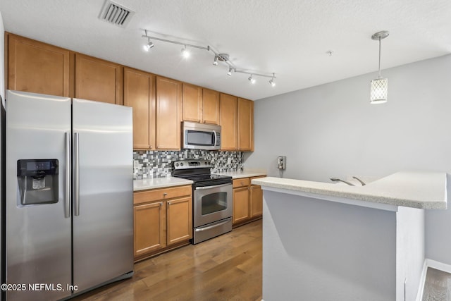kitchen with stainless steel appliances, wood finished floors, light countertops, and backsplash