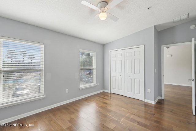 unfurnished bedroom with a closet, wood finished floors, lofted ceiling, baseboards, and ceiling fan