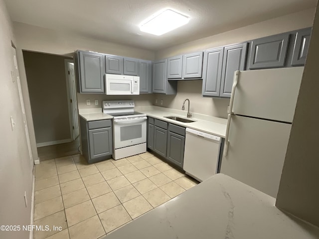kitchen featuring white appliances, light countertops, gray cabinets, a sink, and light tile patterned floors