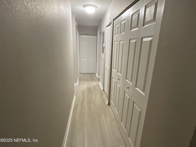 hall featuring baseboards, a textured wall, and light wood finished floors