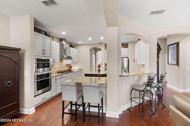 kitchen with dark wood-style flooring, a kitchen breakfast bar, visible vents, and wall chimney exhaust hood