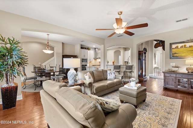 living room featuring ceiling fan, arched walkways, baseboards, visible vents, and hardwood / wood-style flooring