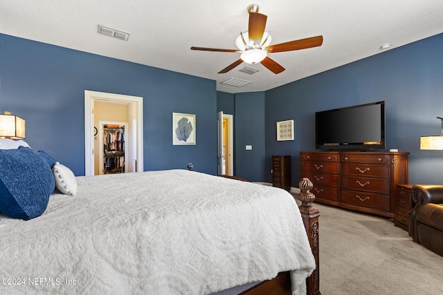 bedroom with ceiling fan, visible vents, light carpet, and a walk in closet