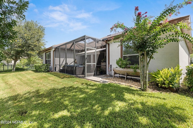 rear view of house with fence, glass enclosure, stucco siding, and a yard