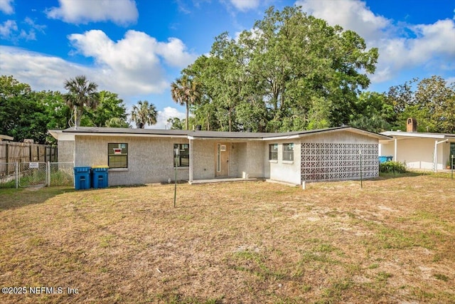 rear view of property with a lawn, fence, and stucco siding
